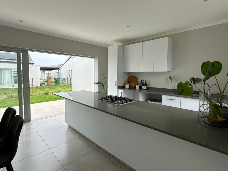 Modern kitchen featuring a large island with a built-in gas hob, stone countertops, sleek cabinetry, and seamless access to the outdoor patio area.