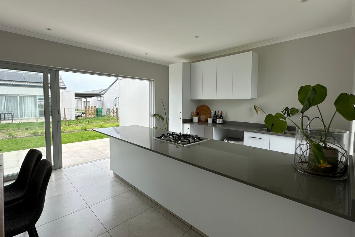 Modern kitchen featuring a large island with a built-in gas hob, stone countertops, sleek cabinetry, and seamless access to the outdoor patio area.
