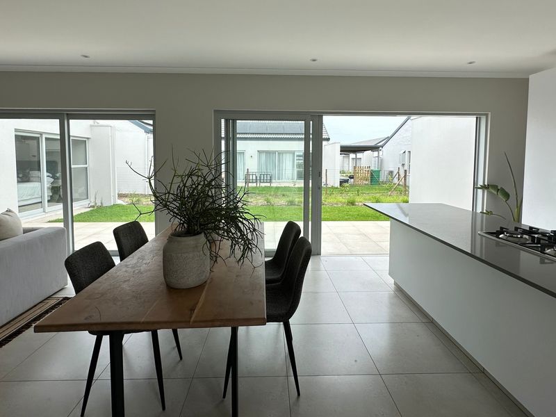 Modern open-plan living and kitchen area featuring large sliding glass doors, a central kitchen island with gas cooktop, and neutral tiled flooring.