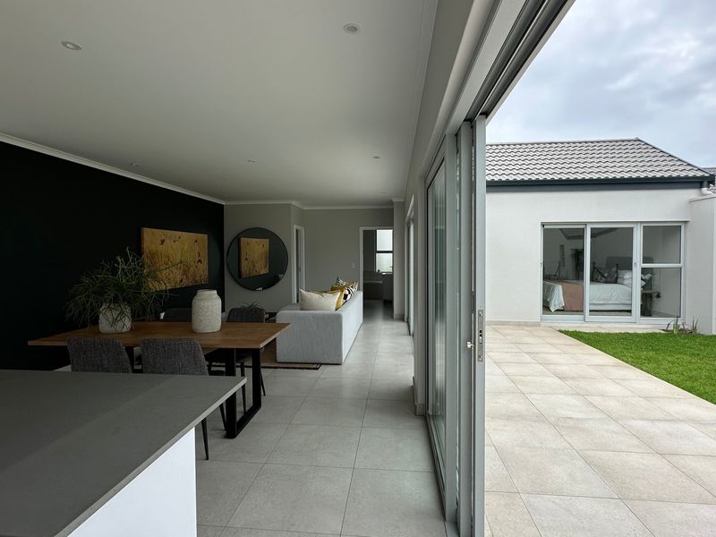 Modern open-plan living area featuring seamless indoor-outdoor flow through large sliding glass doors to a paved patio and garden.
