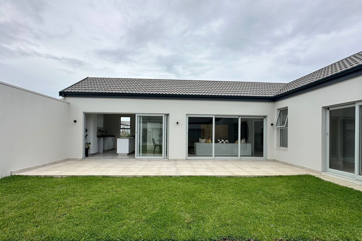Rear view of the property featuring a paved patio area, well-maintained lawn, and large sliding glass doors providing seamless indoor-outdoor flow.