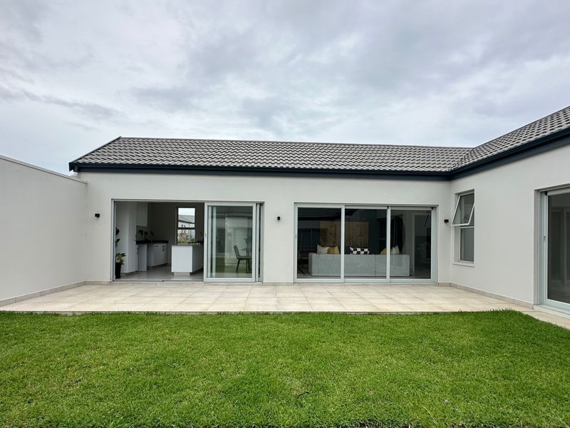 Rear view of the property featuring a paved patio area, well-maintained lawn, and large sliding glass doors providing seamless indoor-outdoor flow.