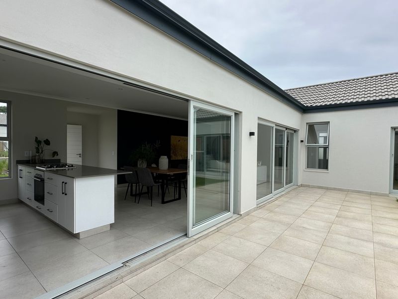 A modern covered patio featuring large sliding glass doors that open into a contemporary open-plan kitchen and living area with tiled flooring.