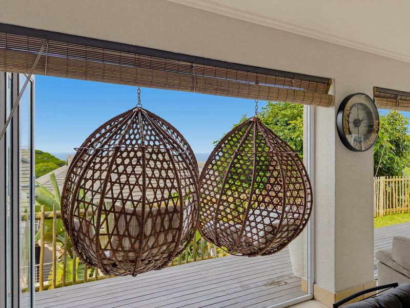 A covered balcony featuring timber decking and bifold doors, offering an open-air feel with views of the surrounding greenery.