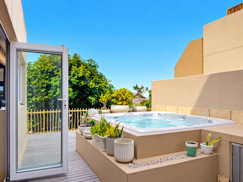 A private outdoor terrace featuring a built-in spa, timber decking, and a glass door entrance, offering a relaxing and well-maintained exterior space.