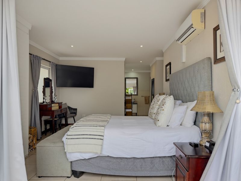 A well-maintained bedroom featuring tiled flooring, recessed ceiling lighting, and a wall-mounted air conditioning unit, with an adjoining view into the bathroom area.