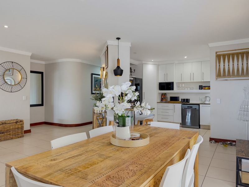 A bright open-plan living and dining area featuring tiled floors, modern kitchen cabinetry with integrated appliances, and recessed lighting throughout.