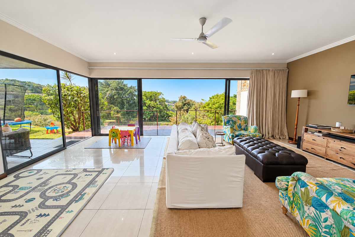 Spacious living room featuring large sliding glass doors that open to an outdoor area, polished tile flooring, and a ceiling fan.