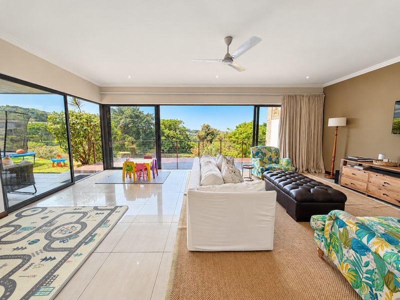 Spacious living room featuring large sliding glass doors that open to an outdoor area, polished tile flooring, and a ceiling fan.