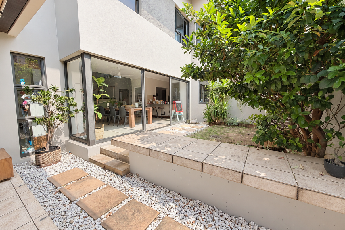 A well-maintained rear exterior featuring a tiled raised planter, stone paver pathway, pebble landscaping, and large sliding glass doors leading into the home.
