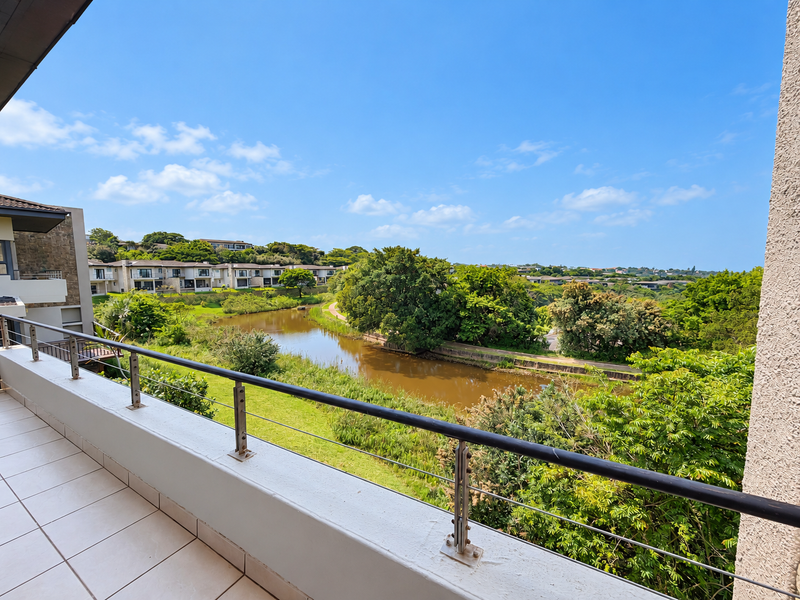 A spacious balcony featuring tiled flooring and a modern stainless steel balustrade, offering scenic views of the surrounding landscape and water feature.
