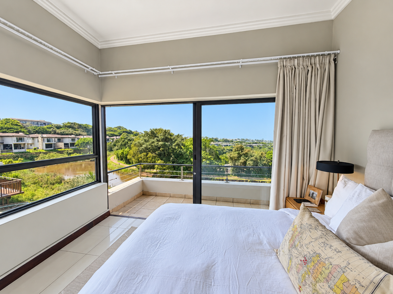 A bright bedroom featuring corner windows and sliding glass doors that open onto a private balcony with scenic views.