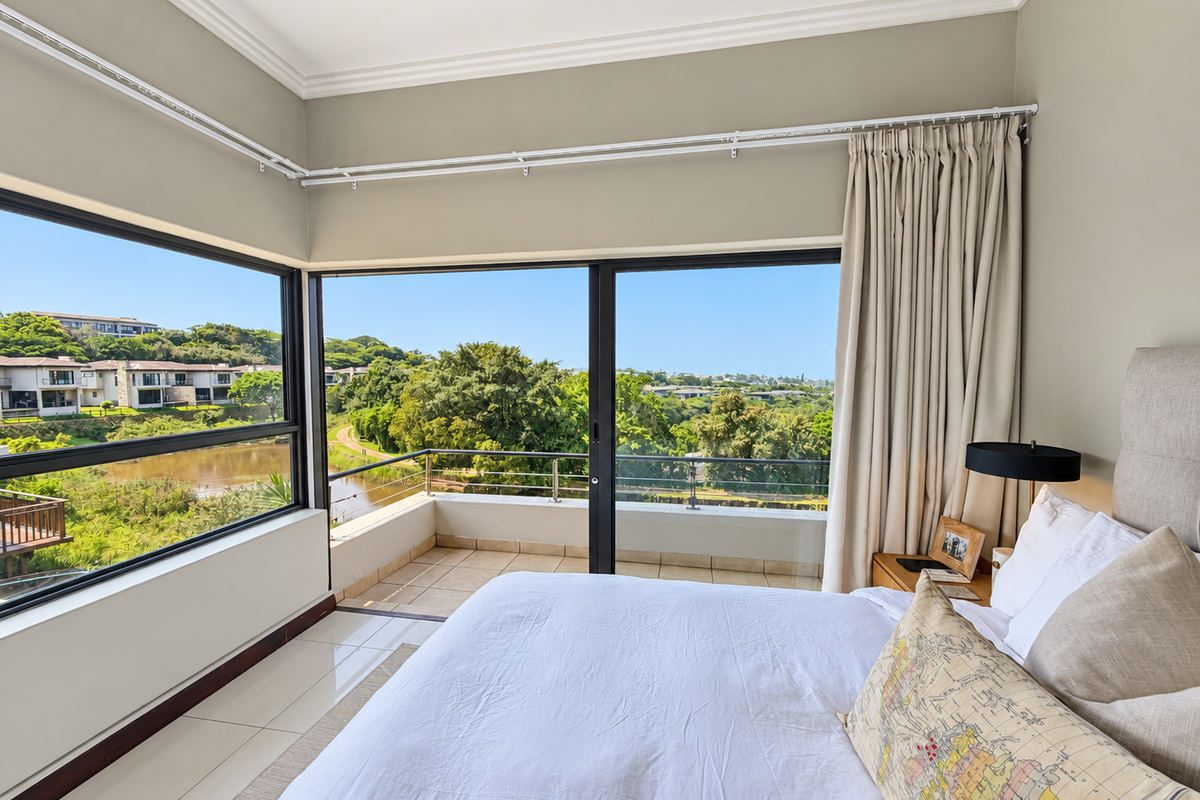 A bright bedroom featuring corner windows and sliding glass doors that open onto a private balcony with scenic views.