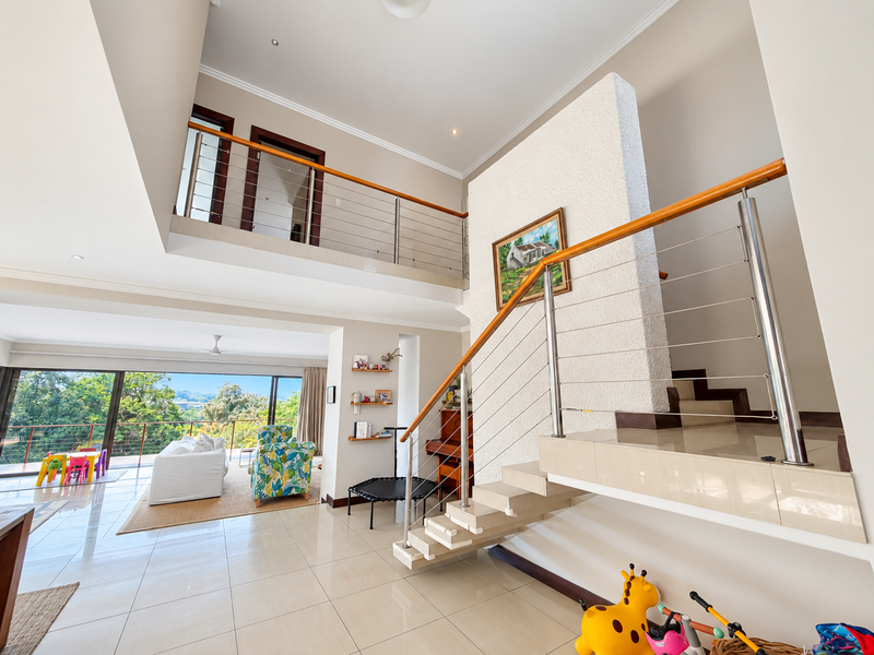 Spacious open-plan living area featuring a modern staircase with stainless steel balustrades, tiled flooring, and large sliding doors leading to an outdoor balcony.