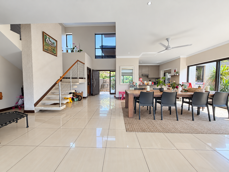 Spacious open-plan living and dining area featuring high ceilings, large windows, modern porcelain tiles, and a striking floating staircase leading to the upper level.