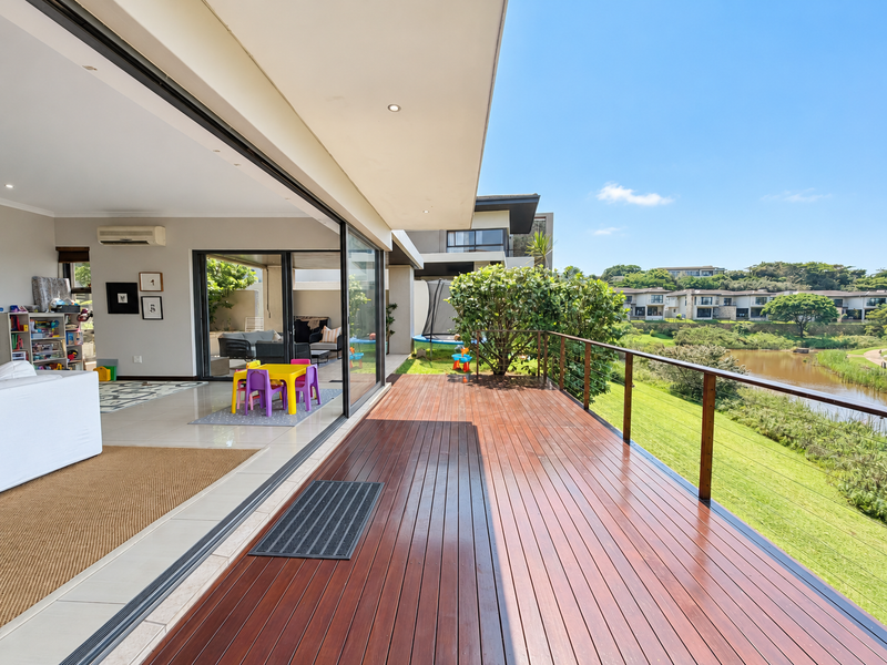 Spacious timber deck balcony featuring stainless steel cable railings, recessed lighting, and seamless indoor-outdoor flow through large sliding glass doors overlooking the estate.