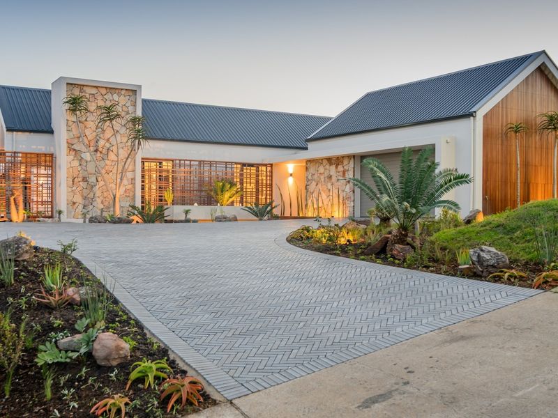 Modern architectural home featuring a herringbone paved driveway, stone and timber facade accents, and a well-maintained landscaped garden at dusk.
