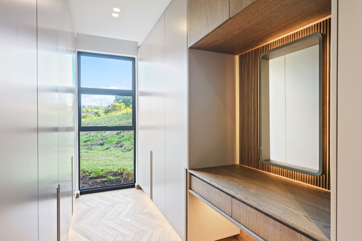 A modern, high-end dressing area or bedroom walk-in closet featuring custom built-in cabinetry, herringbone timber flooring, and a sleek integrated vanity with accent lighting.
