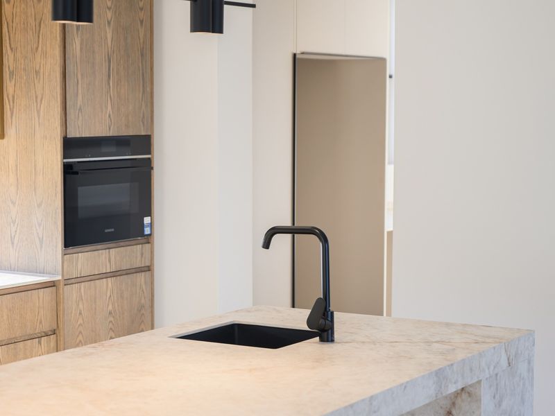 Modern kitchen featuring a stone island with a black faucet, integrated cabinetry, and built-in appliances, showcasing a clean and contemporary design.