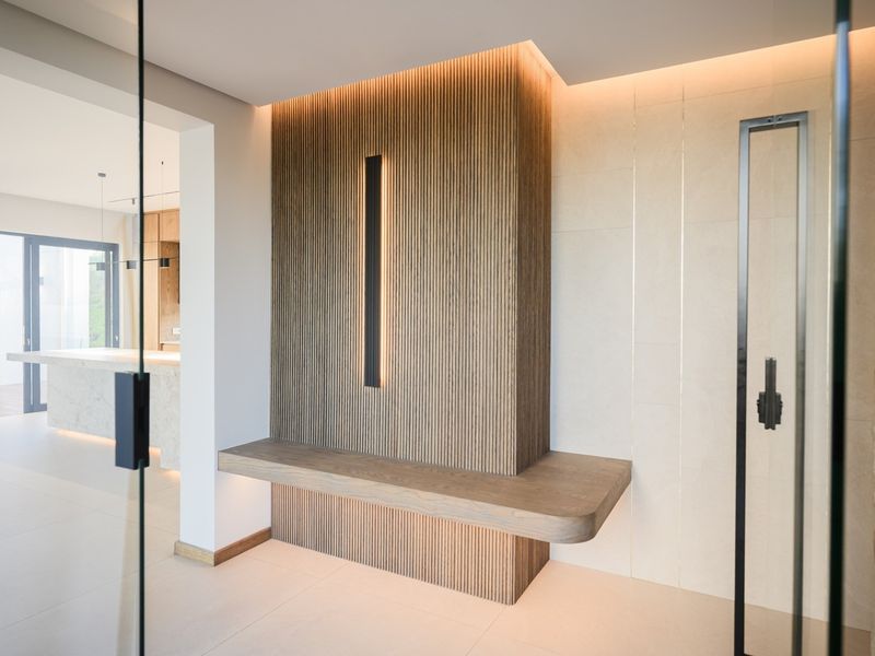 Modern entrance foyer featuring elegant timber slat wall paneling, a floating bench, integrated lighting, and a natural stone feature wall.