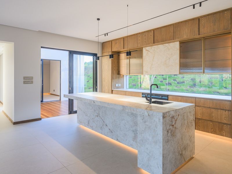 Modern kitchen featuring a large stone island, high-end built-in cabinetry, integrated appliances, and seamless access to an outdoor patio area.