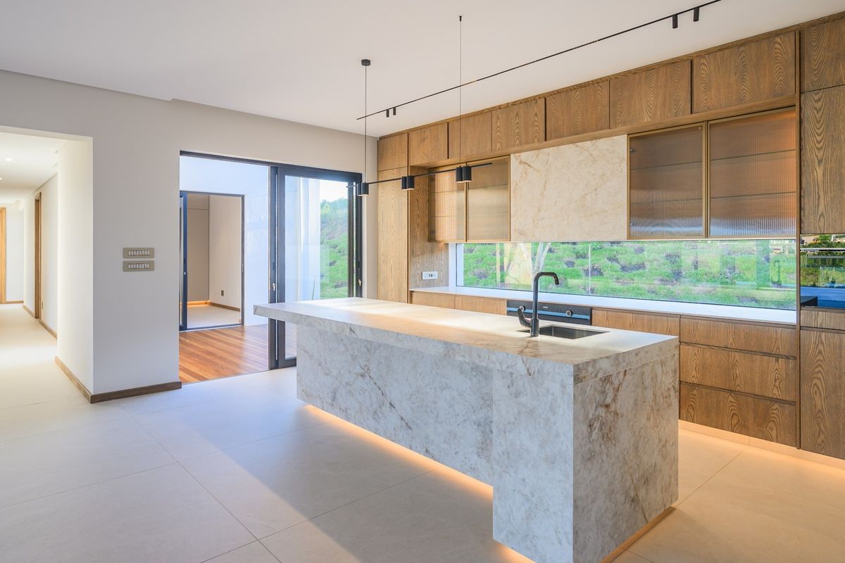 Modern kitchen featuring a large stone island, high-end built-in cabinetry, integrated appliances, and seamless access to an outdoor patio area.
