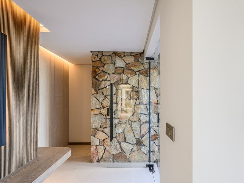 Modern entrance foyer featuring a striking natural stone wall, timber slat detailing, and elegant recessed lighting, creating a sophisticated and welcoming transition space.