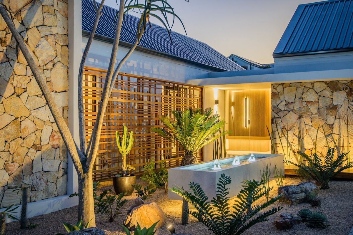 A beautifully landscaped rear courtyard featuring stone-clad walls, a modern water feature, and architectural timber screening with integrated ambient lighting.