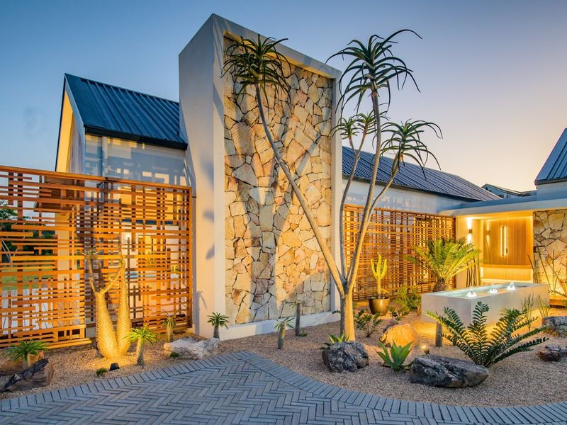 Modern architectural front facade featuring stone cladding, timber screening, and a landscaped garden with a built-in water feature.