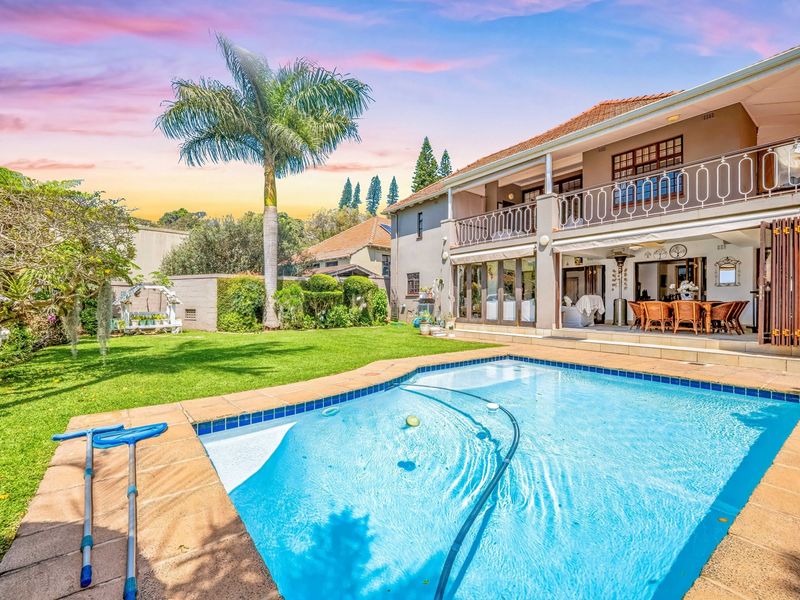 Spacious rear garden featuring a well-maintained swimming pool, paved patio area, and a two-story home with a balcony overlooking the outdoor space.