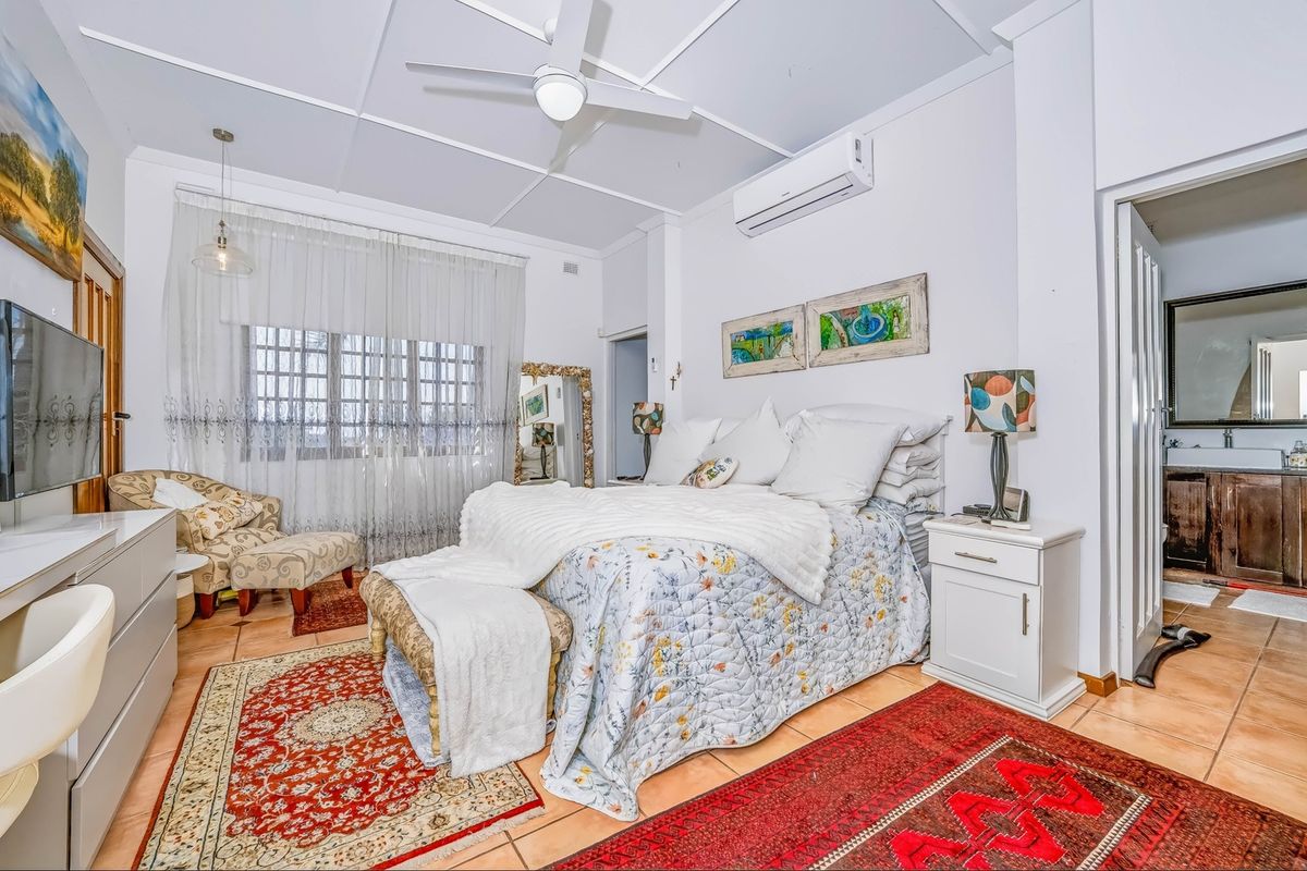 A well-lit bedroom featuring tiled flooring, a ceiling fan, and a split-system air conditioner, with direct access to an en-suite bathroom.