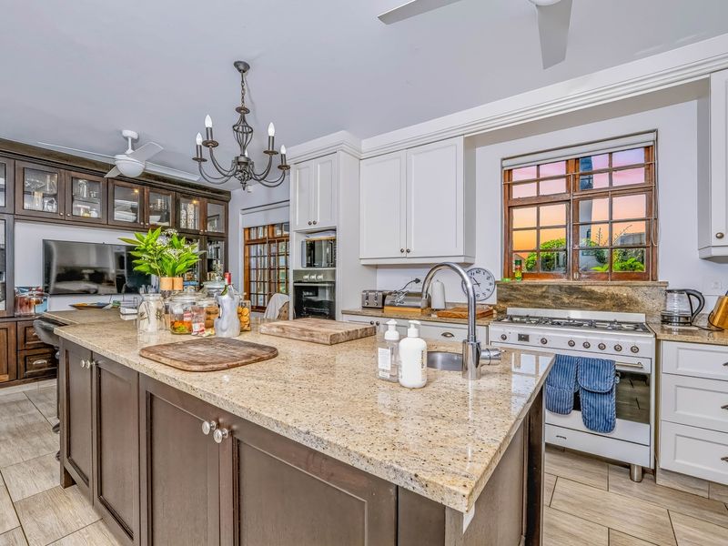 A well-appointed kitchen featuring a large granite-topped island, custom cabinetry, built-in gas stove, and tiled flooring, offering a functional and classic design.