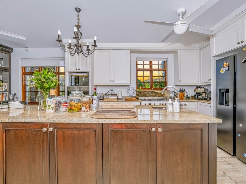 A well-appointed kitchen featuring a large granite-topped island, ample built-in cabinetry, a gas hob, and a ceiling fan, offering a functional and classic design.