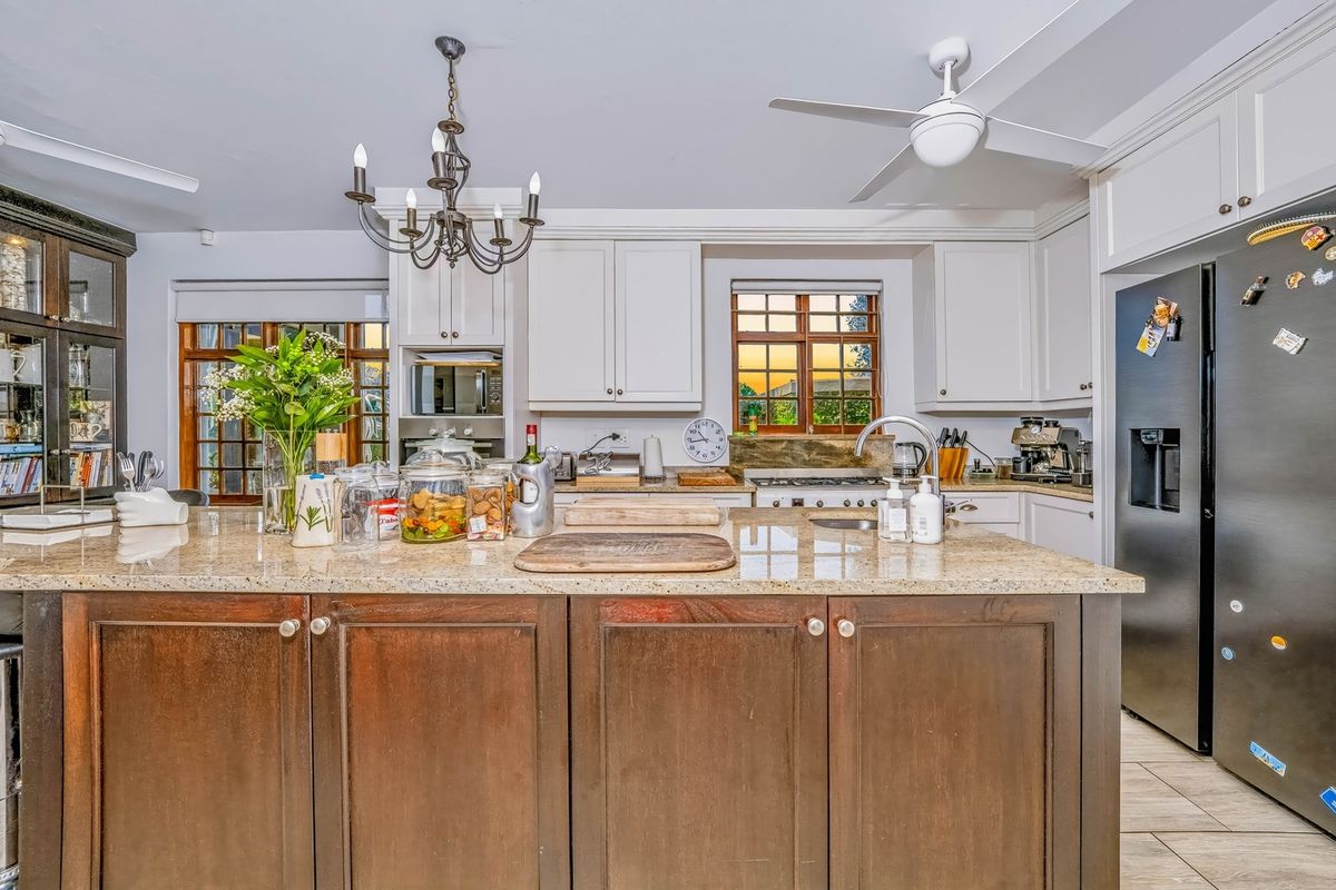 A well-appointed kitchen featuring a large granite-topped island, ample built-in cabinetry, a gas hob, and a ceiling fan, offering a functional and classic design.