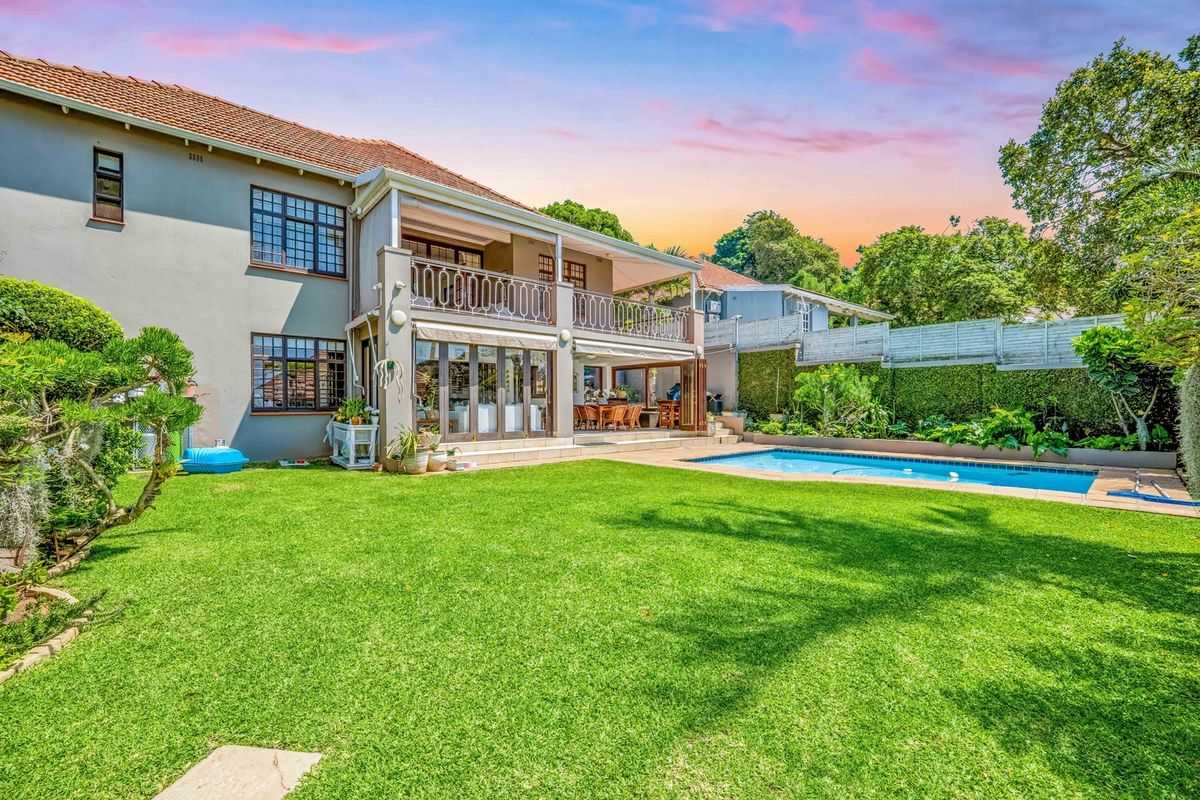 Spacious rear garden featuring a swimming pool, a covered patio area, and an upper-level balcony with wrought iron detailing.