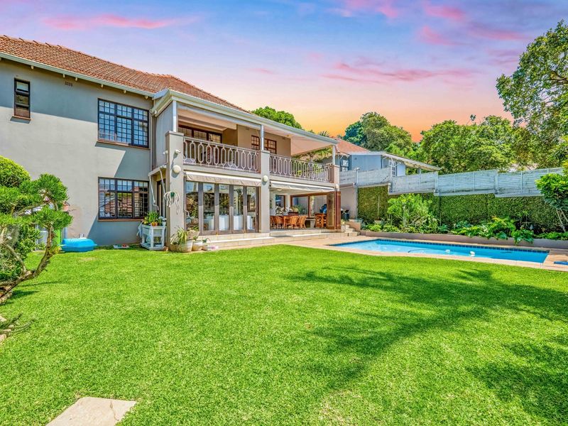 Spacious rear garden featuring a swimming pool, a covered patio area, and an upper-level balcony with wrought iron detailing.