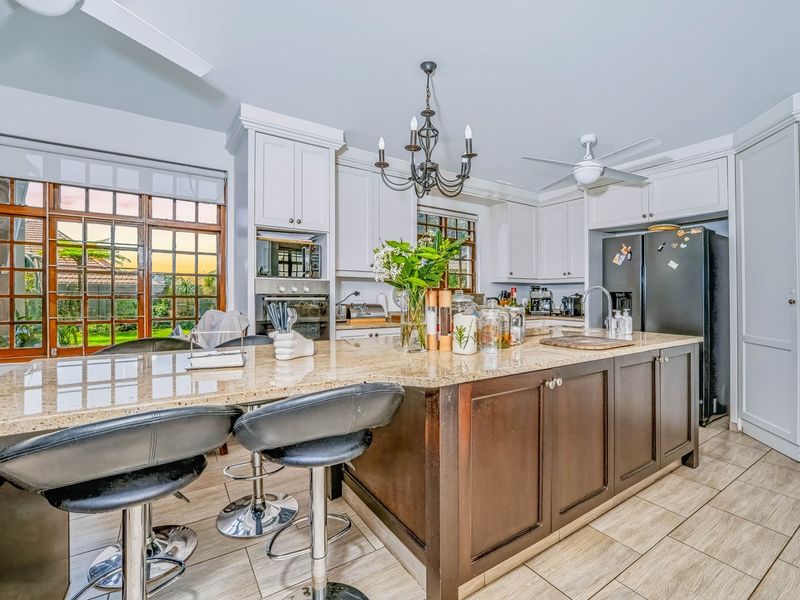 Spacious kitchen featuring a large granite-topped island, built-in appliances, classic cabinetry, and large timber-framed windows overlooking the garden.