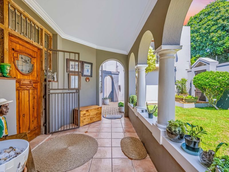 A covered patio area featuring classic arched columns, tiled flooring, and a decorative wooden front door overlooking a well-maintained garden.