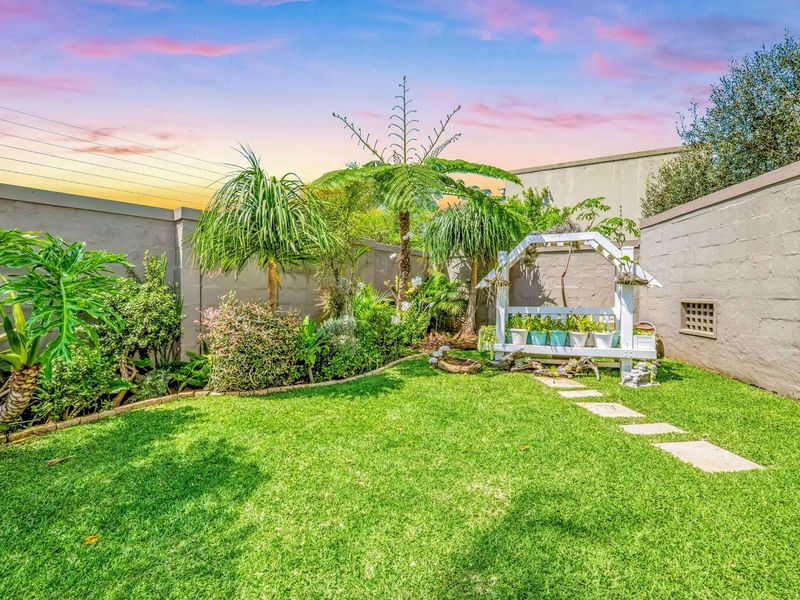 A well-maintained private garden featuring a lush lawn, established landscaping, and a stone paver path enclosed by high perimeter boundary walls.