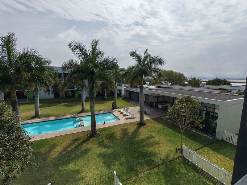 An elevated view of a well-maintained communal pool area featuring a swimming pool, landscaped garden, and a covered patio space.
