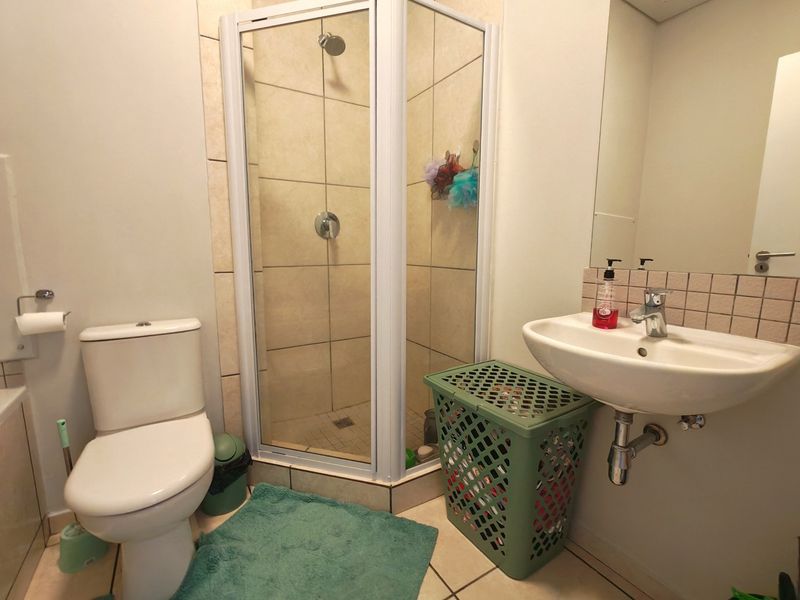 A functional bathroom featuring a corner shower enclosure, a wall-mounted basin with a tiled splashback, and a standard toilet.