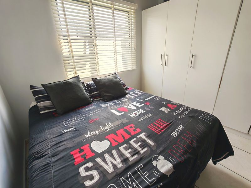 A well-lit bedroom featuring neutral tiled flooring, a functional built-in wardrobe, and venetian blinds for privacy.