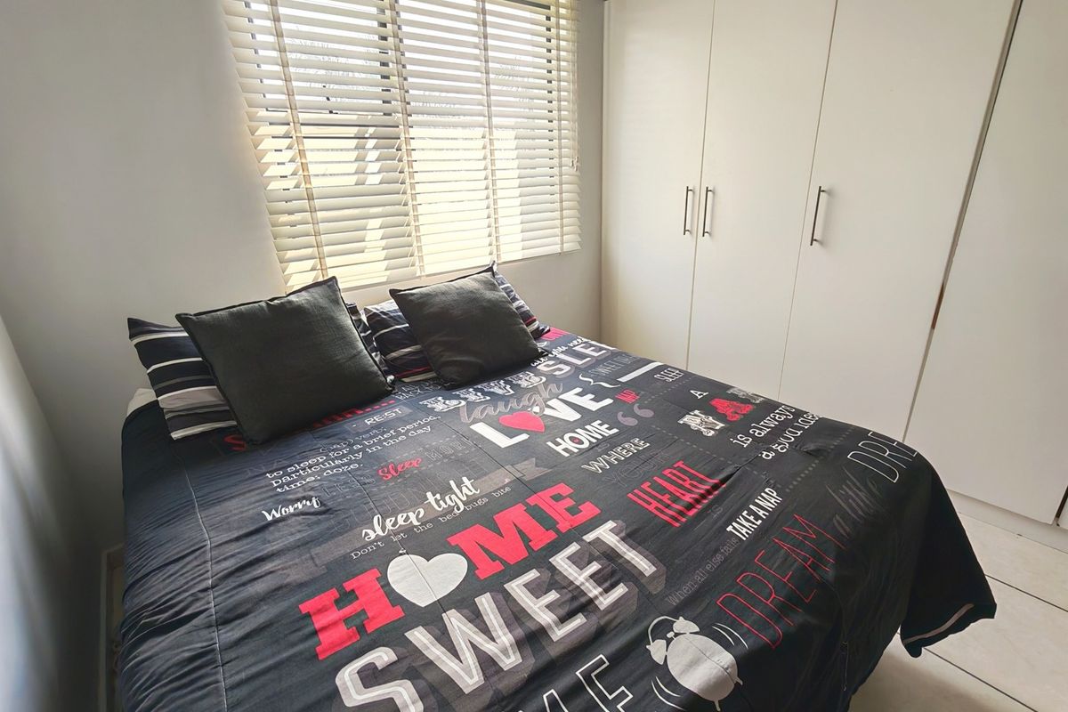 A well-lit bedroom featuring neutral tiled flooring, a functional built-in wardrobe, and venetian blinds for privacy.