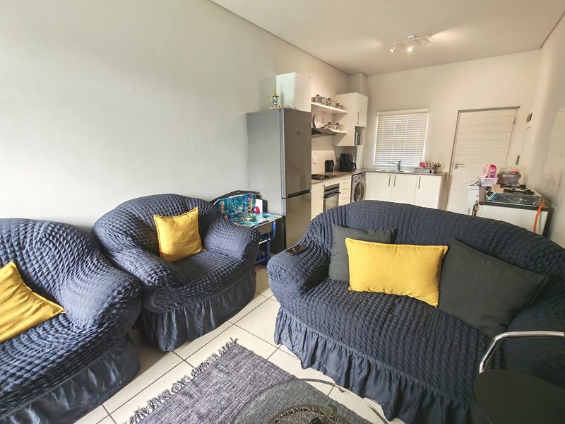 An open-plan living area featuring a compact kitchen with built-in cabinetry, oven, extractor fan, and tiled flooring throughout.