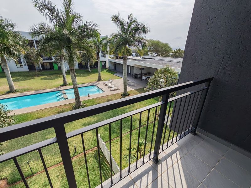 A private balcony overlooking a well-maintained communal garden and swimming pool area within the apartment complex.