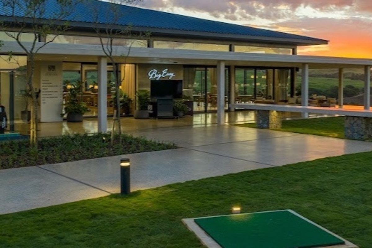 A beautifully maintained rear exterior featuring a spacious covered patio with stone pillars, large glass doors, and a manicured lawn with a putting green.