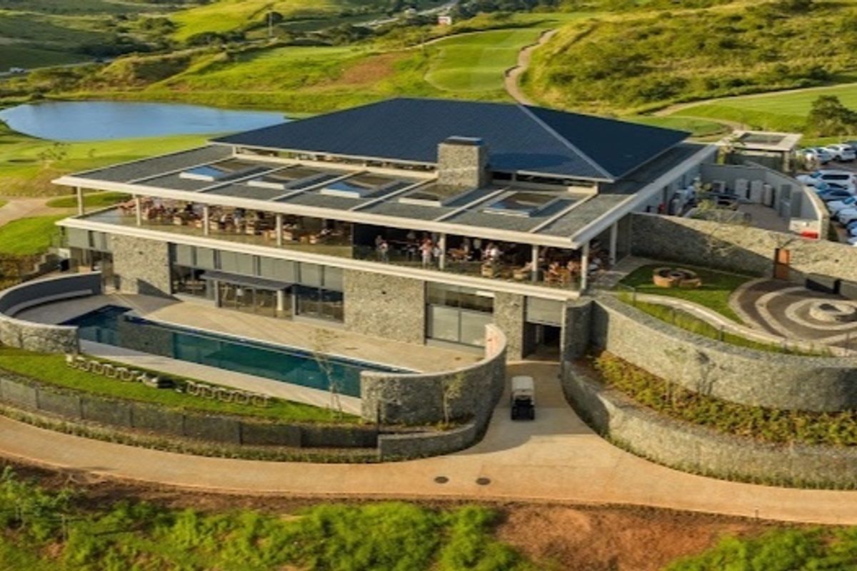 Aerial view of a modern clubhouse featuring stone architecture, a swimming pool, landscaped gardens, and extensive golf course views.