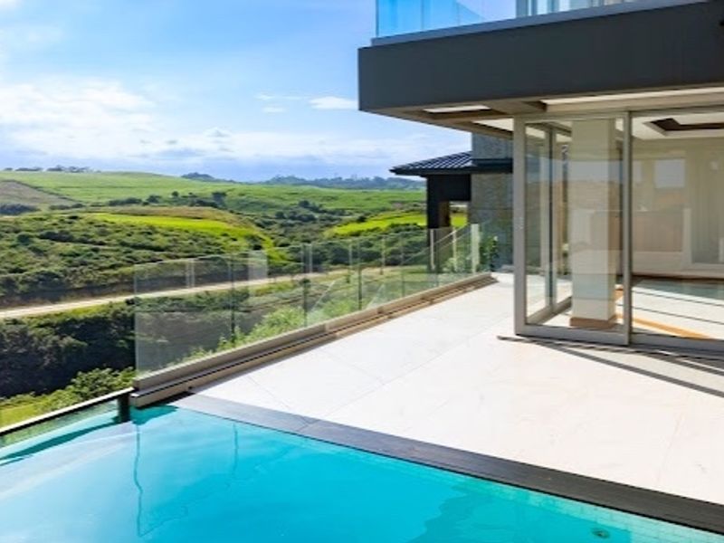 Modern infinity edge swimming pool with a glass balustrade and expansive tiled patio, offering scenic views of the surrounding landscape.