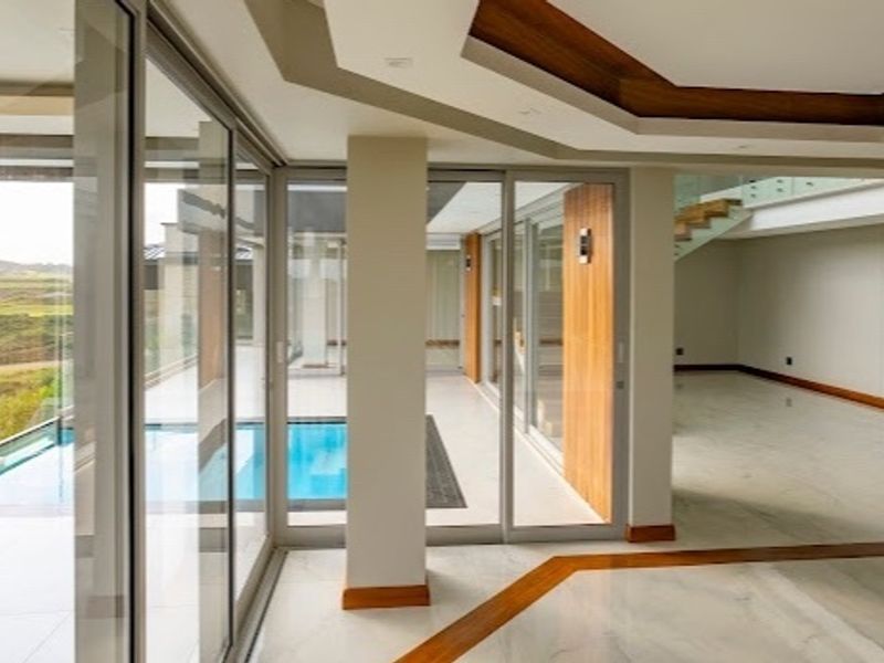 Spacious open-plan living area featuring high-end marble flooring, recessed ceilings with wood accents, and large sliding glass doors opening to a private swimming pool.