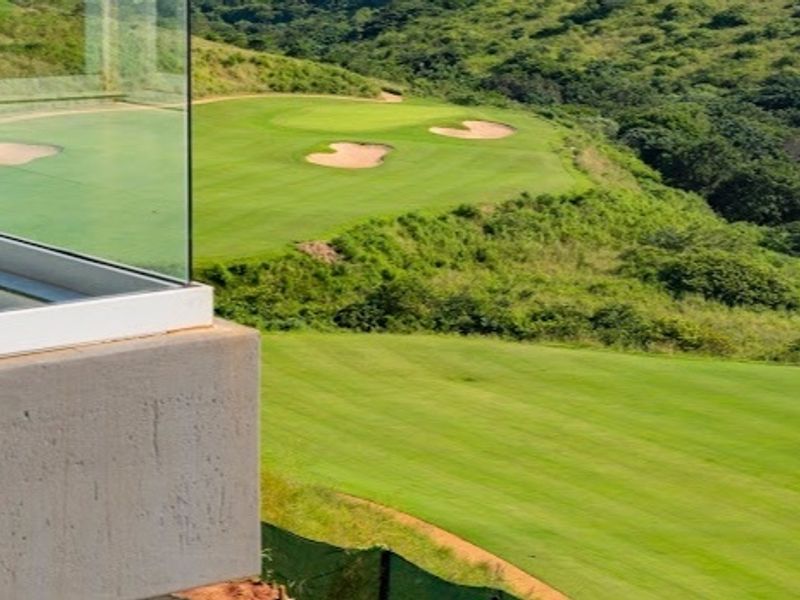A scenic view overlooking a lush green golf course from a modern balcony with a glass balustrade.